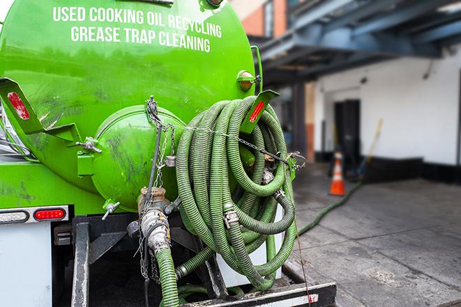 a professional plumber using a pump to empty a grease trap in Palm Springs, FL